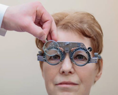 A male optometrist checks the eyesight of an adult woman with a trial frame.
